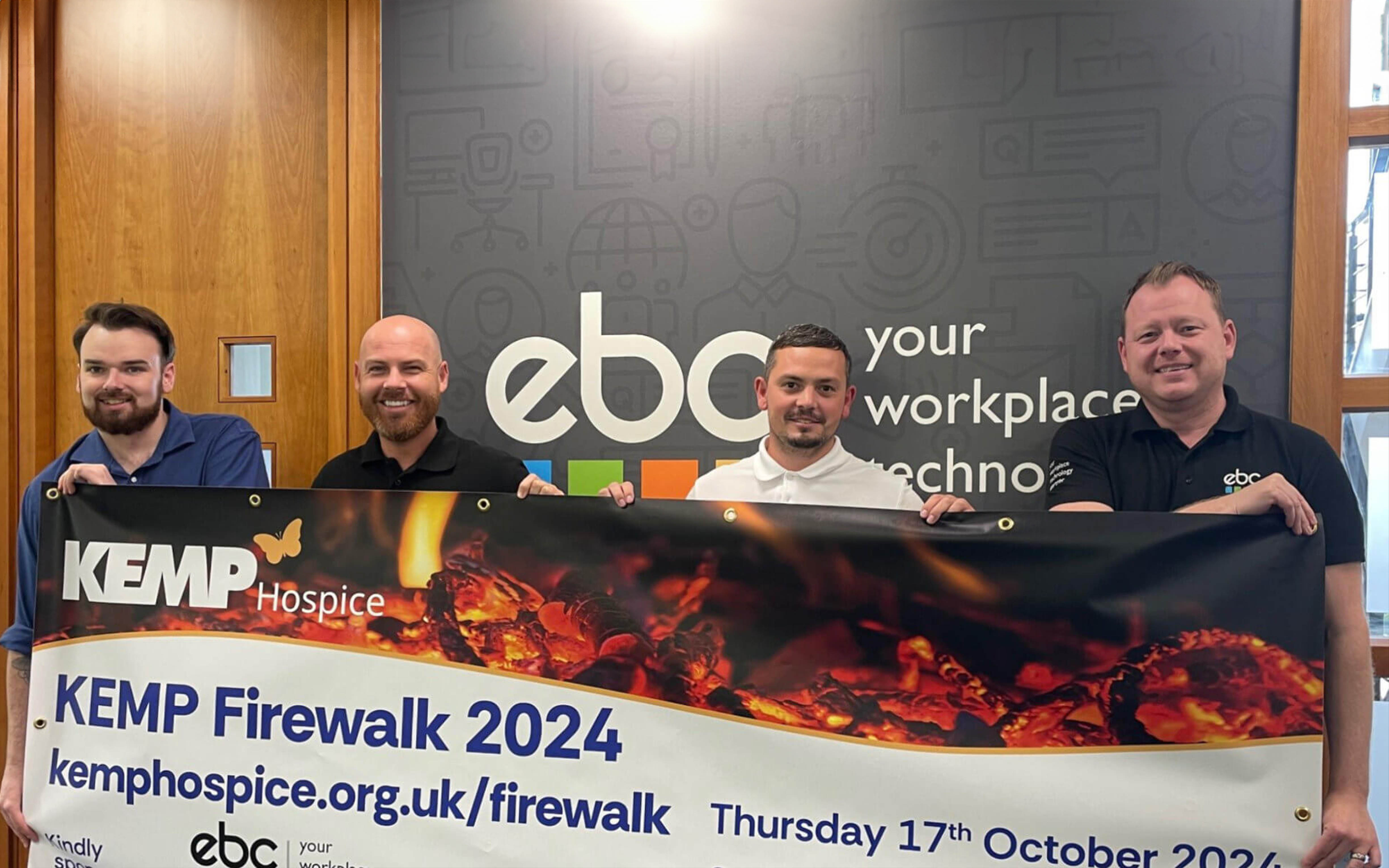 EBC Group staff holding a banner for the KEMP Hospice Firewalk event.